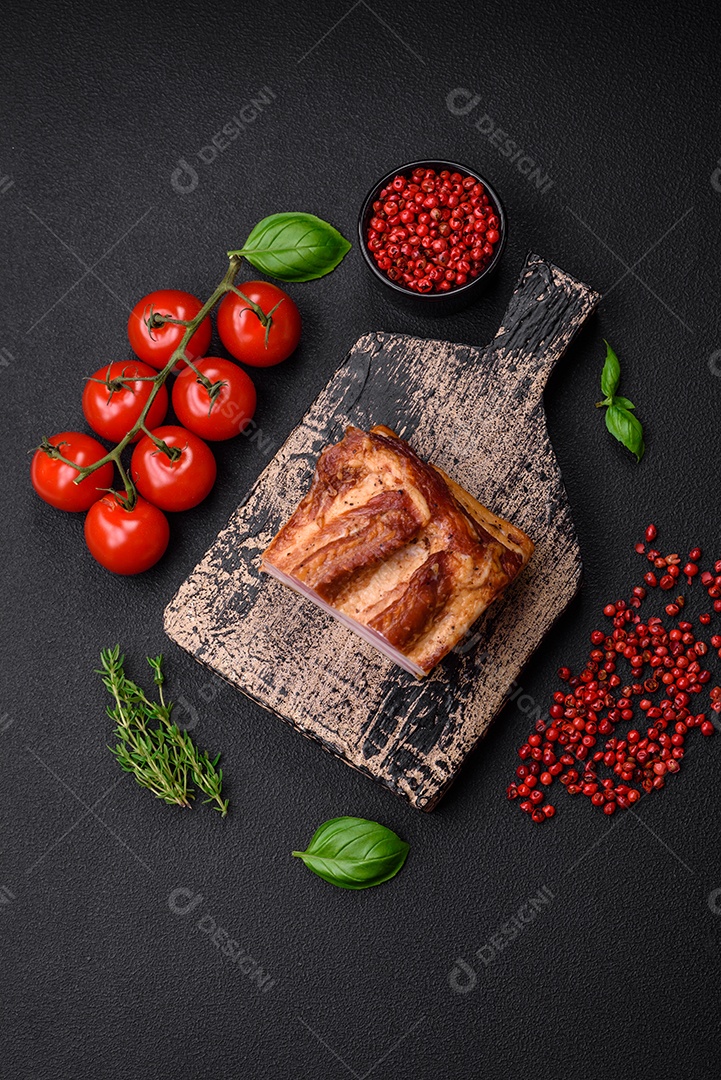 Delicioso bacon defumado com sal, especiarias e ervas sobre um fundo escuro de concreto