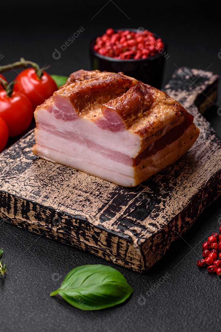 Delicioso bacon defumado com sal, especiarias e ervas sobre um fundo escuro de concreto