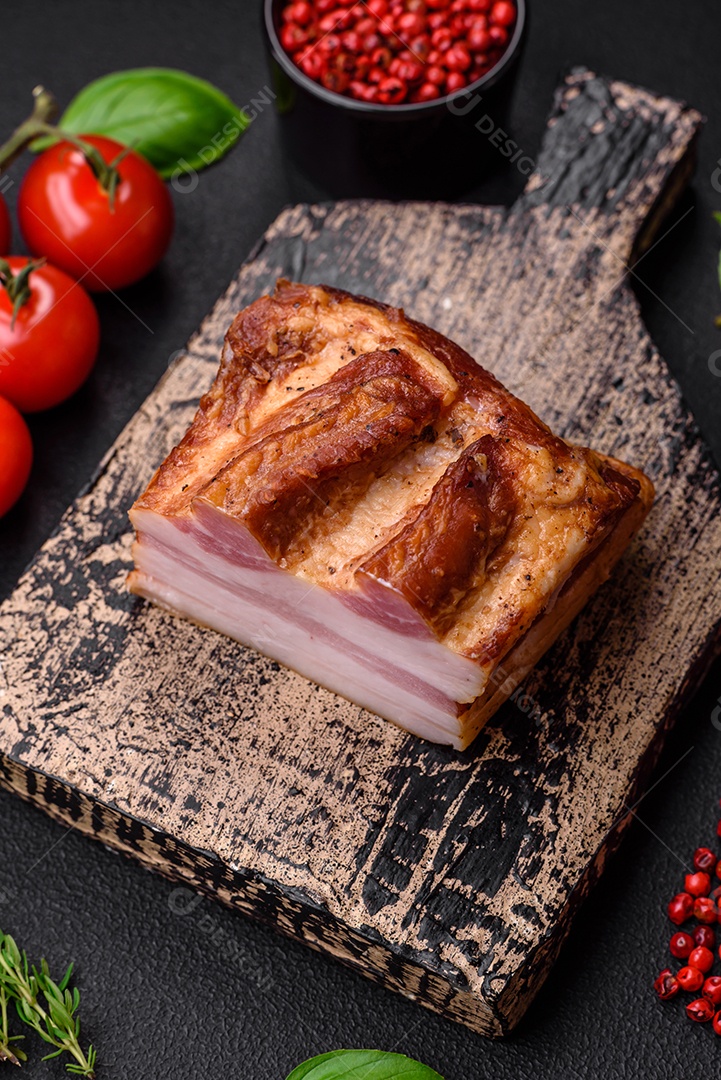 Delicioso bacon defumado com sal, especiarias e ervas sobre um fundo escuro de concreto