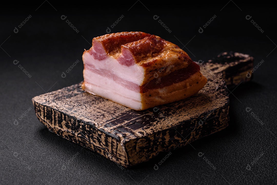 Delicioso bacon defumado com sal, especiarias e ervas sobre um fundo escuro de concreto