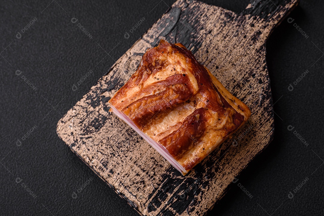 Delicioso bacon defumado com sal, especiarias e ervas sobre um fundo escuro de concreto