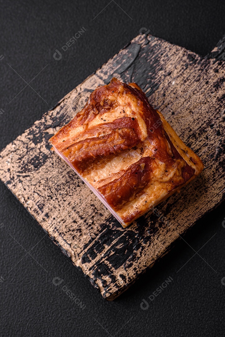Delicioso bacon defumado com sal, especiarias e ervas sobre um fundo escuro de concreto