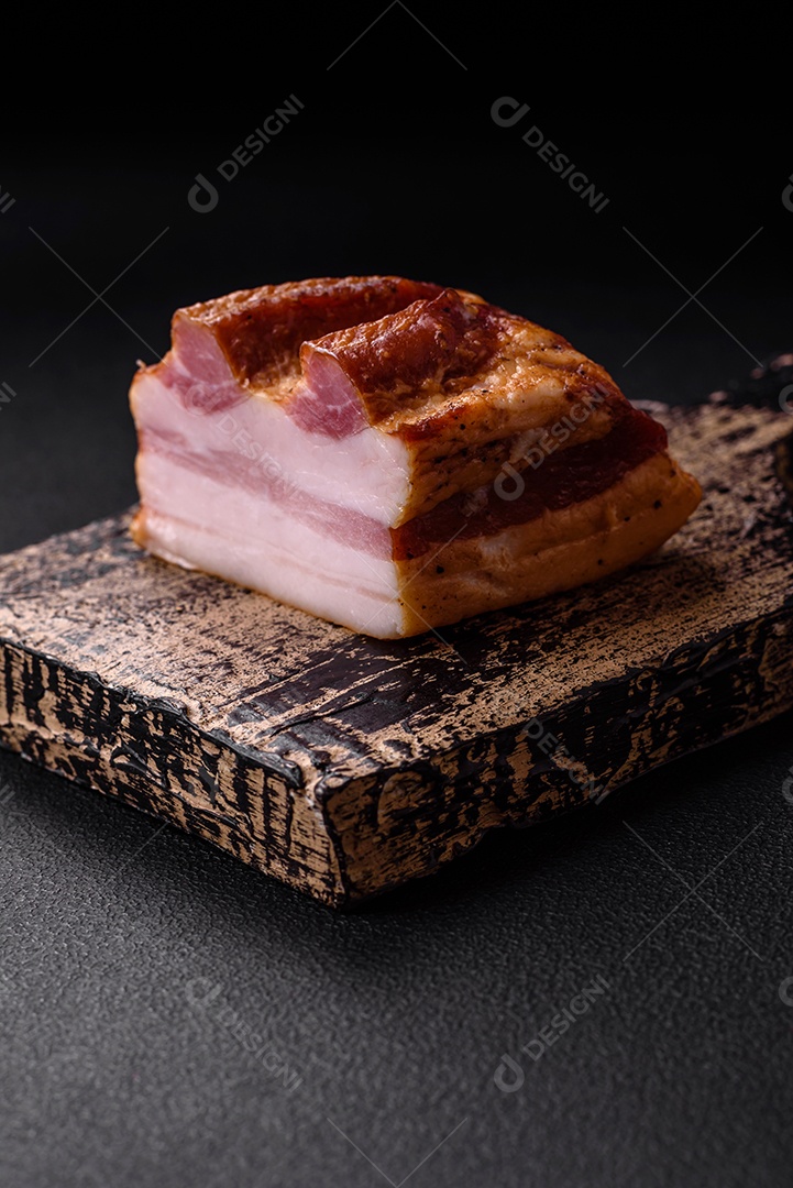 Delicioso bacon defumado com sal, especiarias e ervas sobre um fundo escuro de concreto