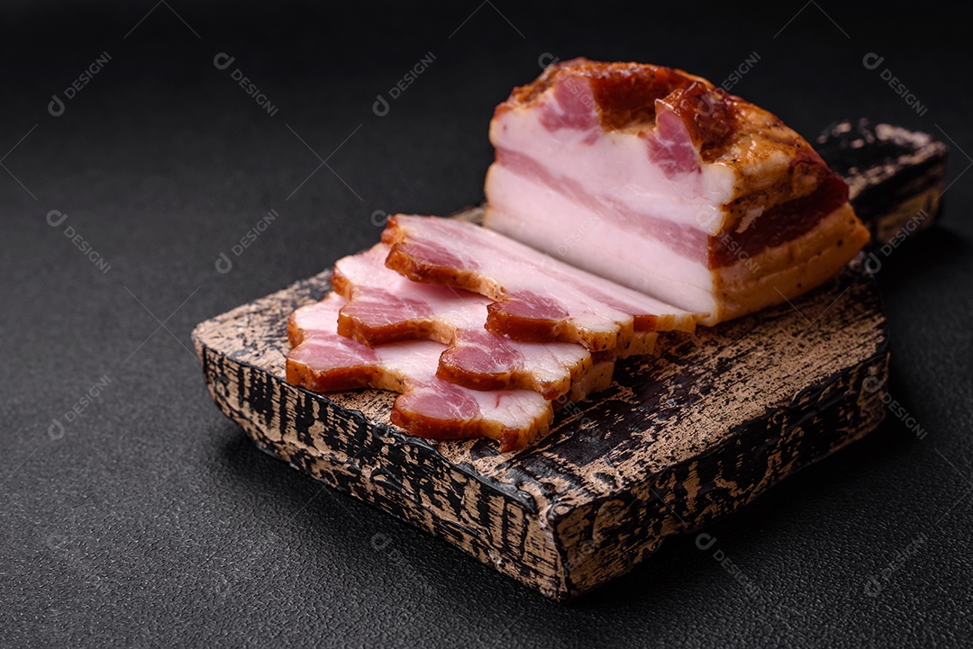 Delicioso bacon defumado com sal, especiarias e ervas sobre um fundo escuro de concreto