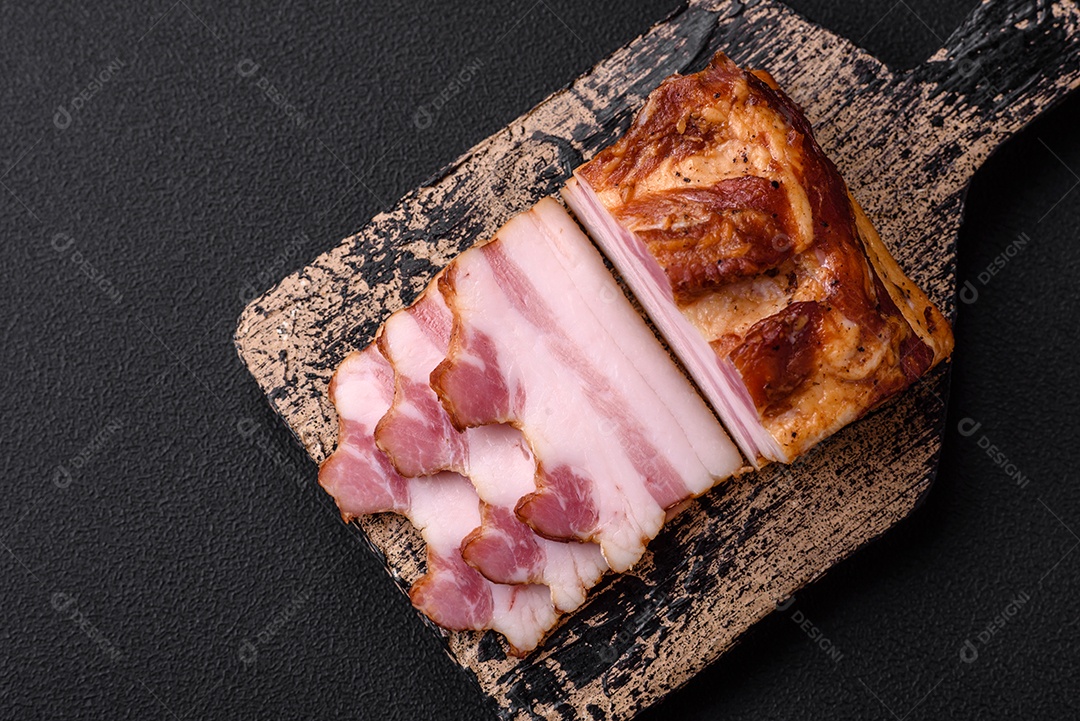 Delicioso bacon defumado com sal, especiarias e ervas sobre um fundo escuro de concreto