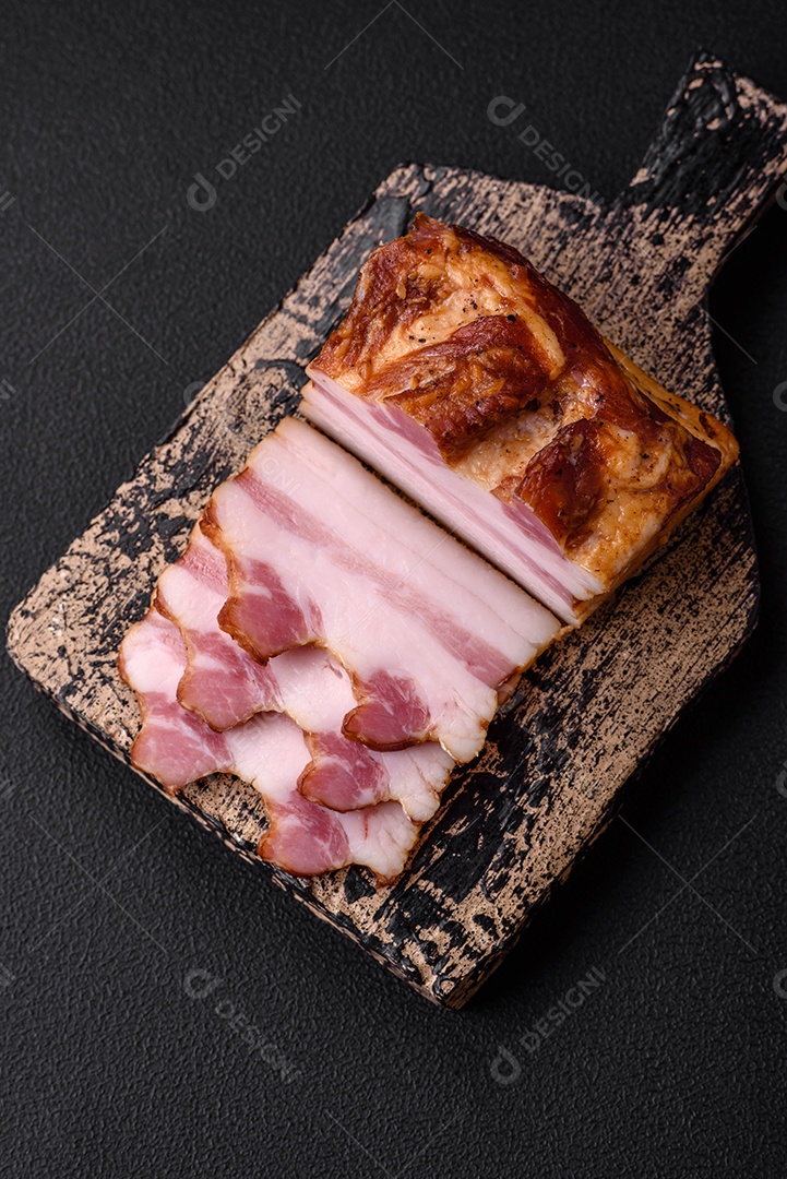 Delicioso bacon defumado com sal, especiarias e ervas sobre um fundo escuro de concreto