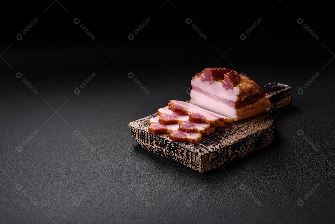Delicioso bacon defumado com sal, especiarias e ervas sobre um fundo escuro de concreto