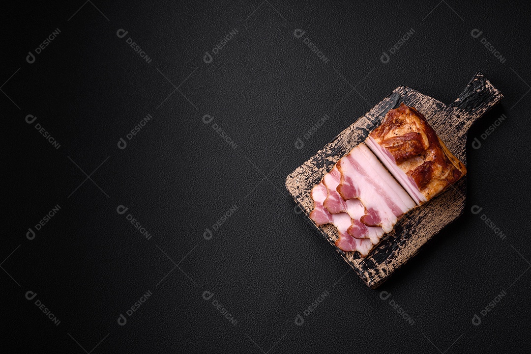 Delicioso bacon defumado com sal, especiarias e ervas sobre um fundo escuro de concreto