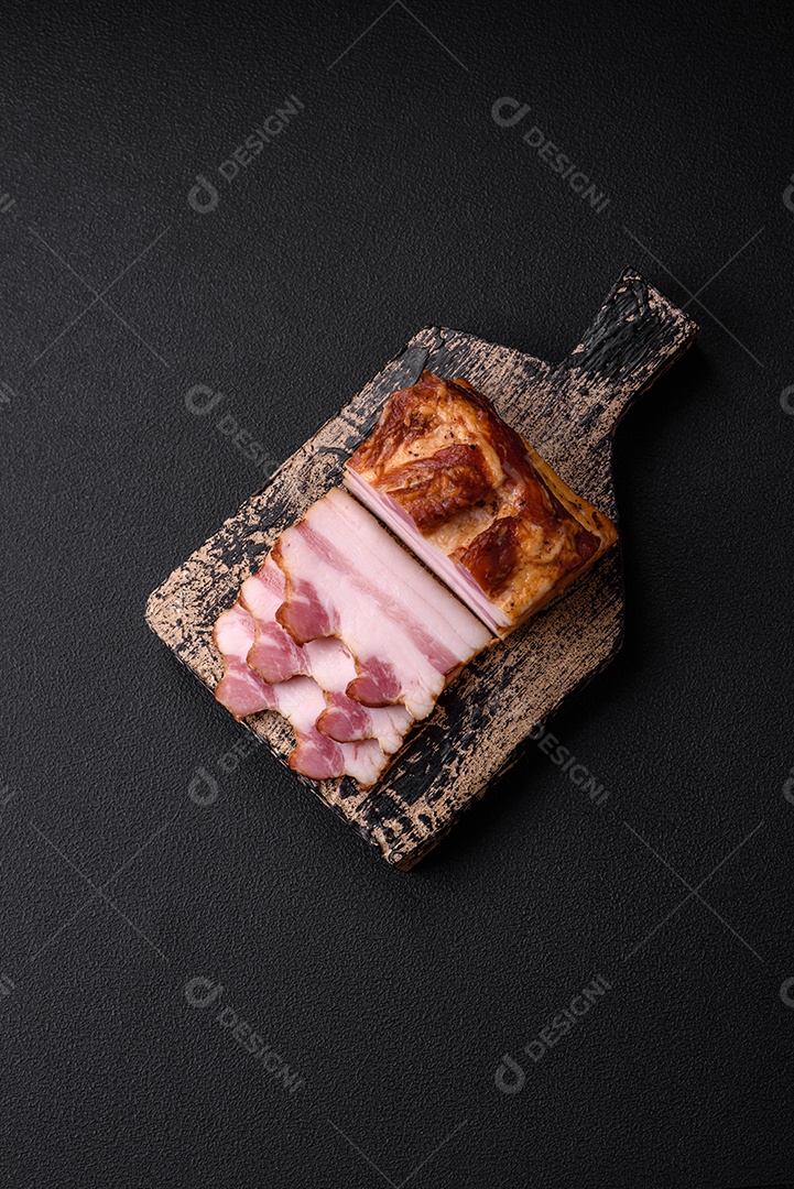Delicioso bacon defumado com sal, especiarias e ervas sobre um fundo escuro de concreto