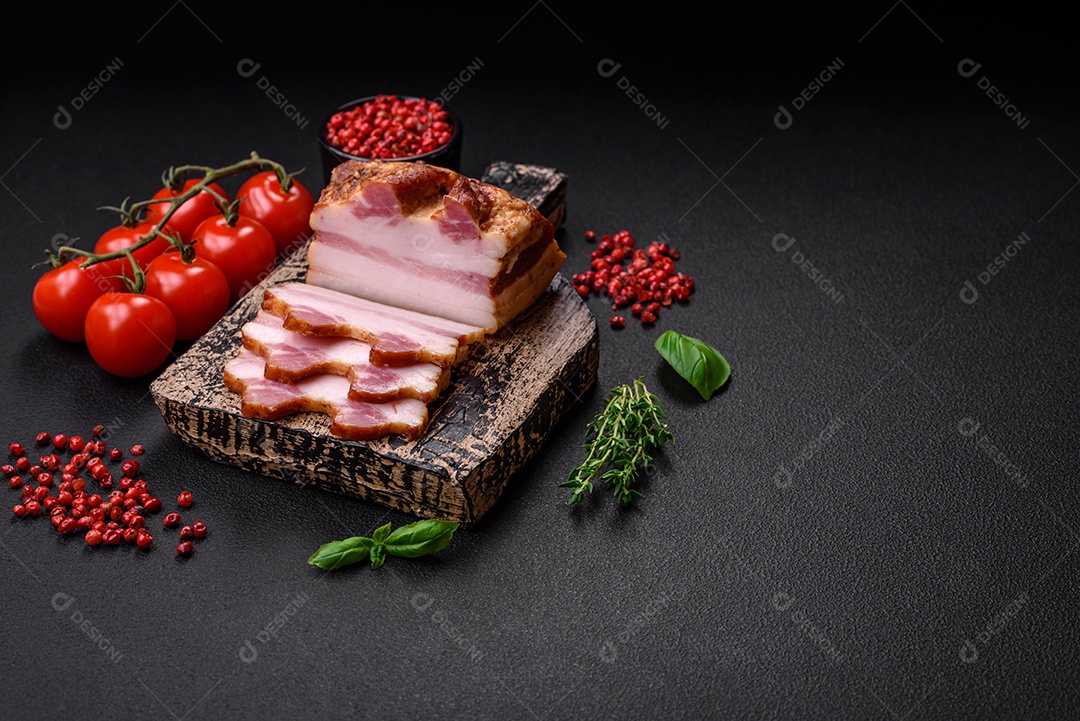 Delicioso bacon defumado com sal, especiarias e ervas sobre um fundo escuro de concreto