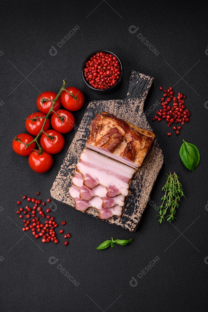 Delicioso bacon defumado com sal, especiarias e ervas sobre um fundo escuro de concreto