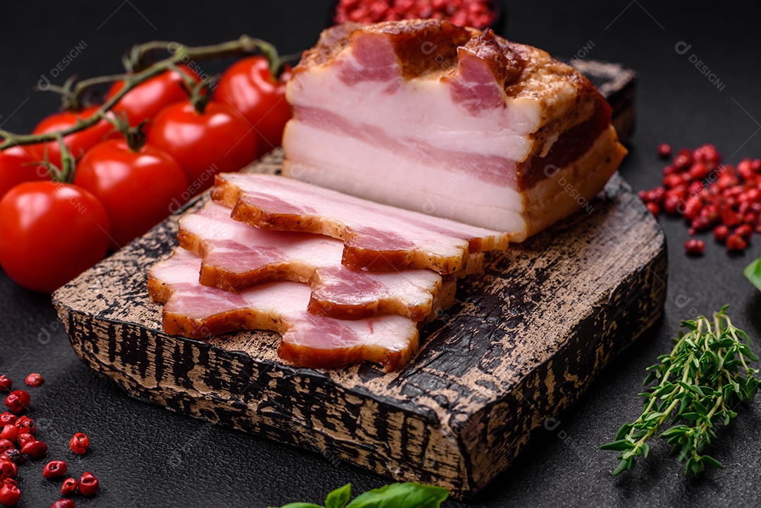 Delicioso bacon defumado com sal, especiarias e ervas sobre um fundo escuro de concreto