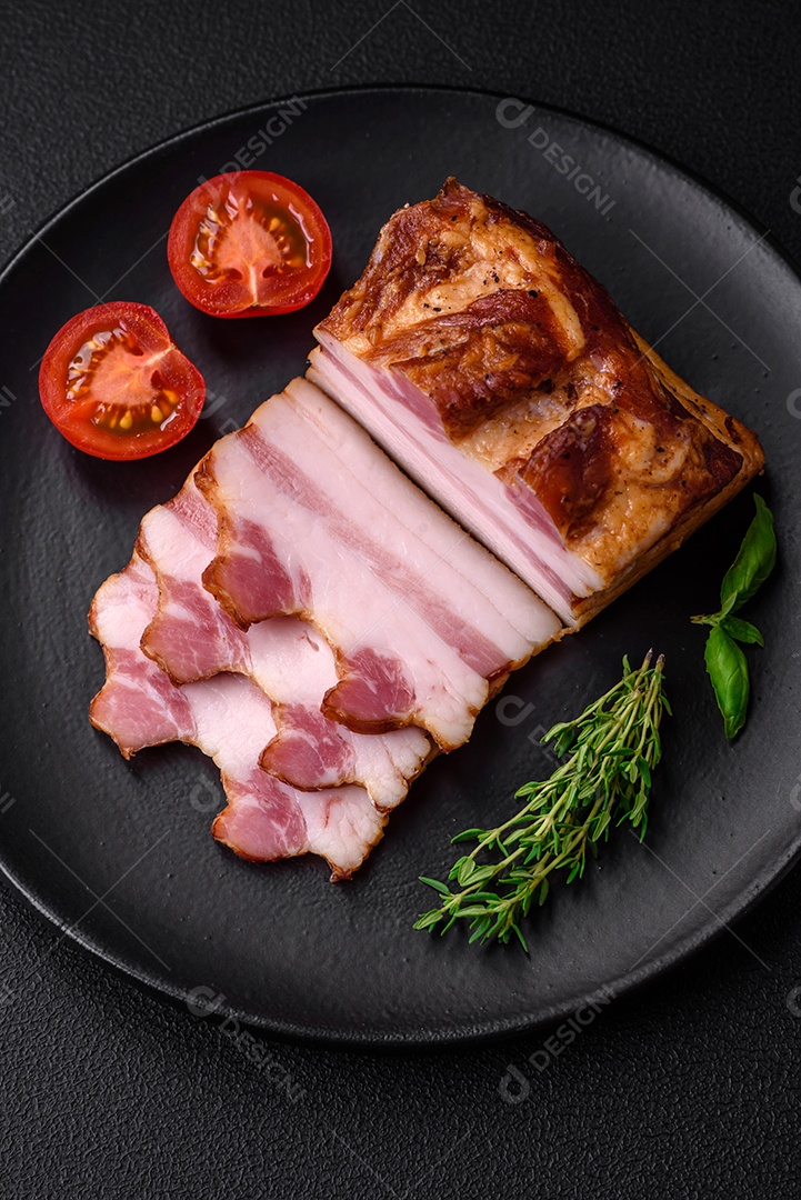 Delicioso bacon defumado com sal, especiarias e ervas sobre um fundo escuro de concreto