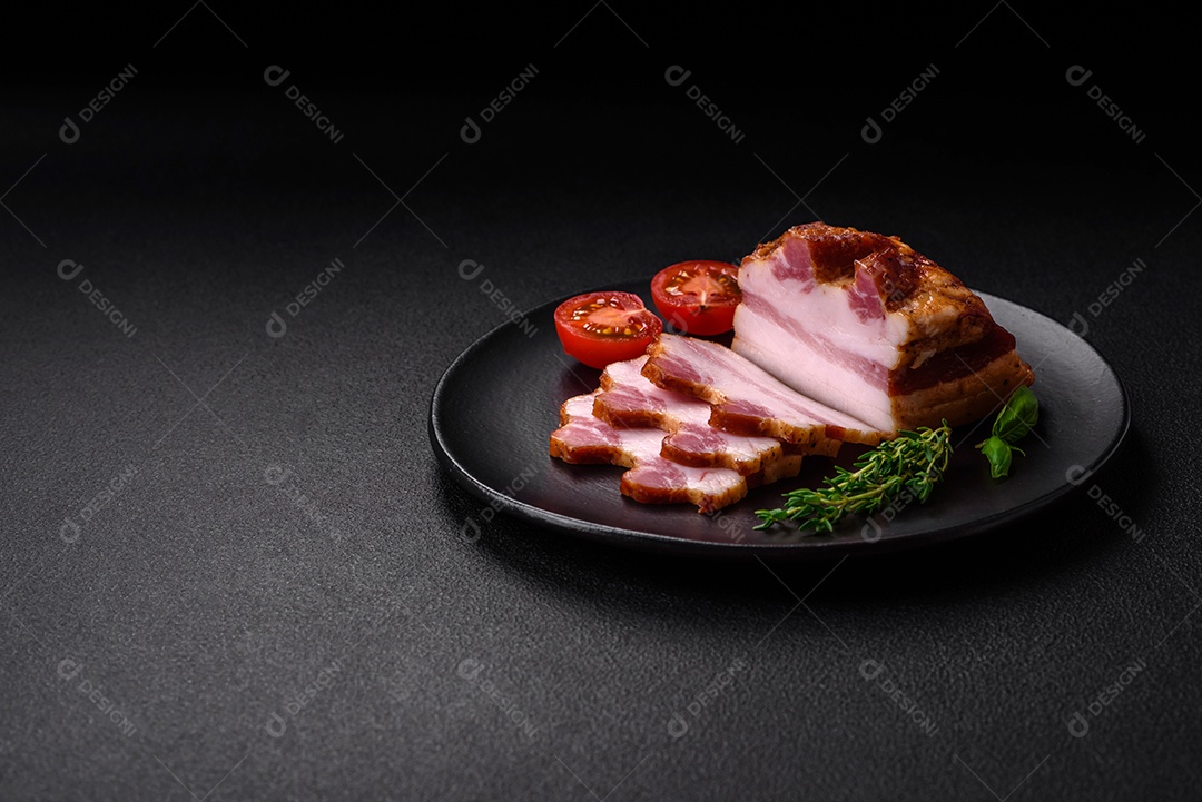 Delicioso bacon defumado com sal, especiarias e ervas sobre um fundo escuro de concreto