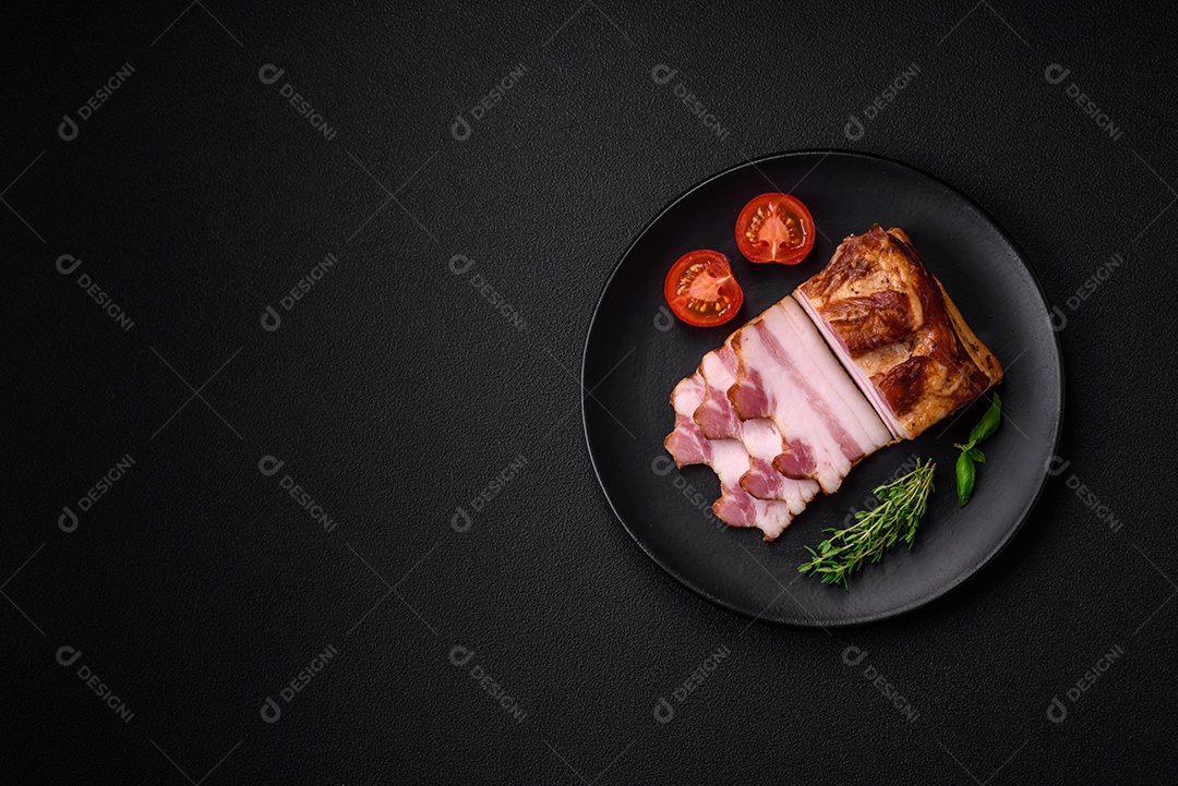 Delicioso bacon defumado com sal, especiarias e ervas sobre um fundo escuro de concreto