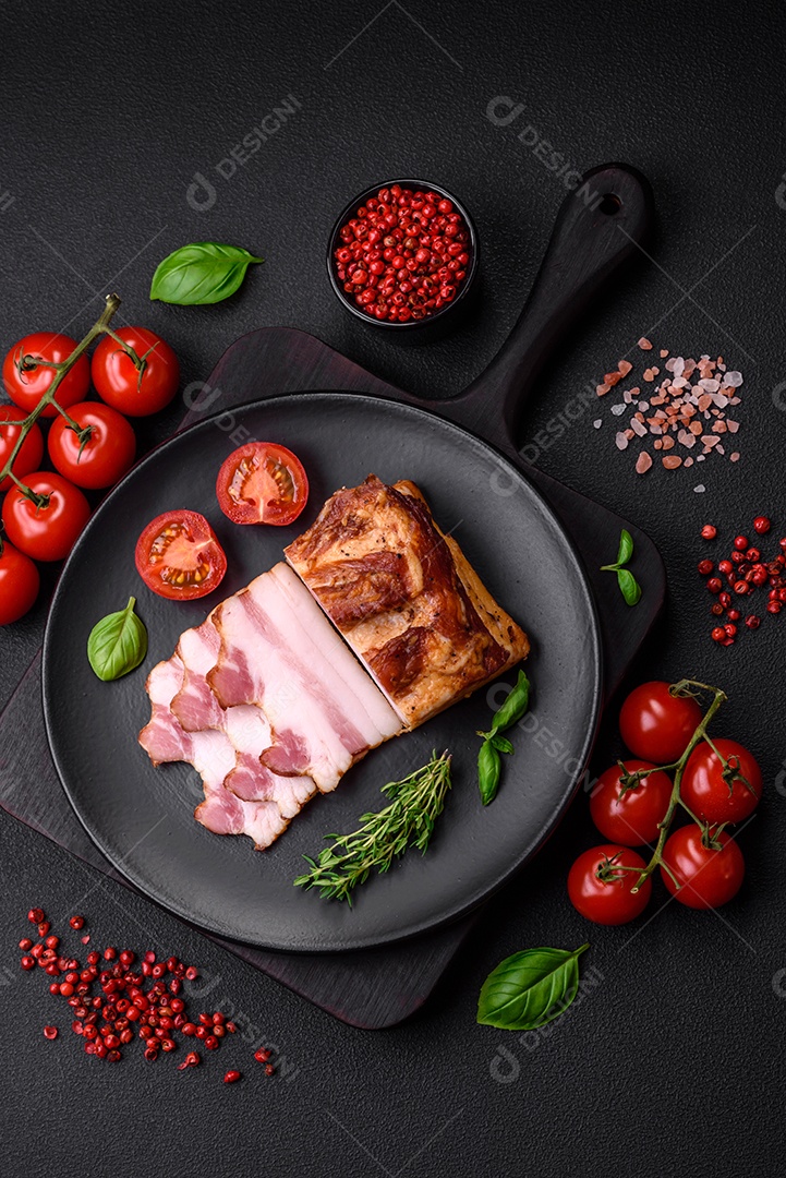 Delicioso bacon defumado com sal, especiarias e ervas sobre um fundo escuro de concreto