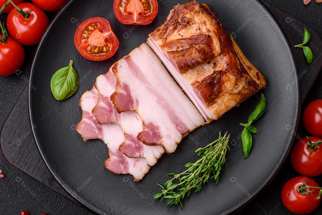 Delicioso bacon defumado com sal, especiarias e ervas sobre um fundo escuro de concreto