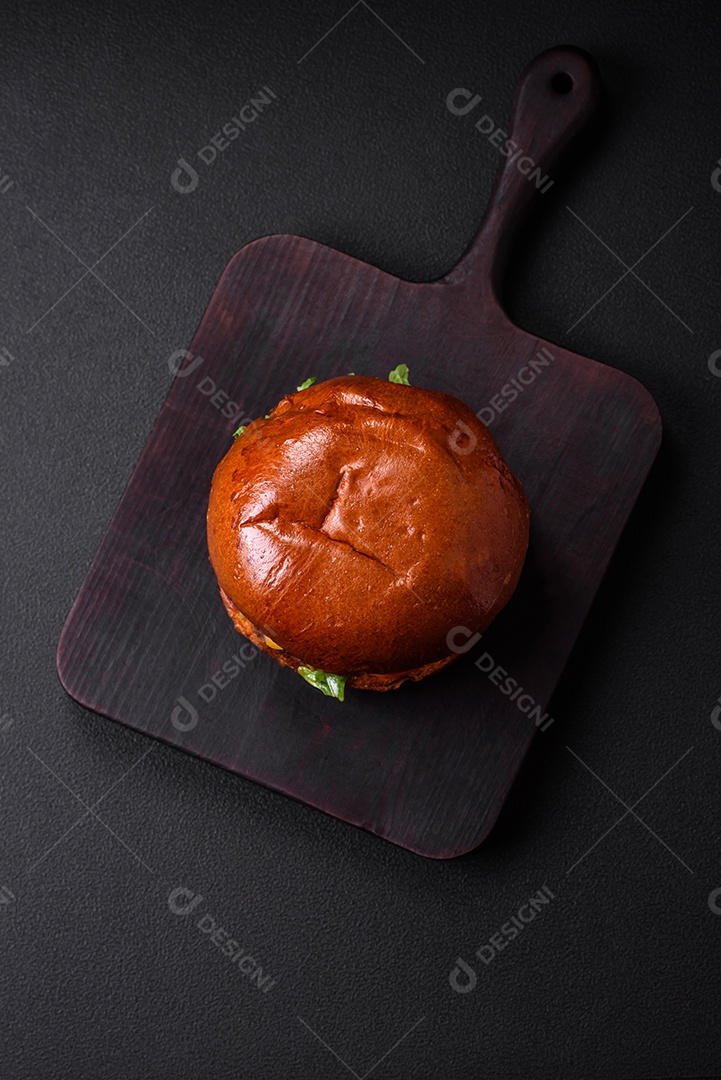 Hambúrguer com suculenta costeleta de carne, queijo, tomate, sal, especiarias e ervas sobre um fundo escuro de concreto