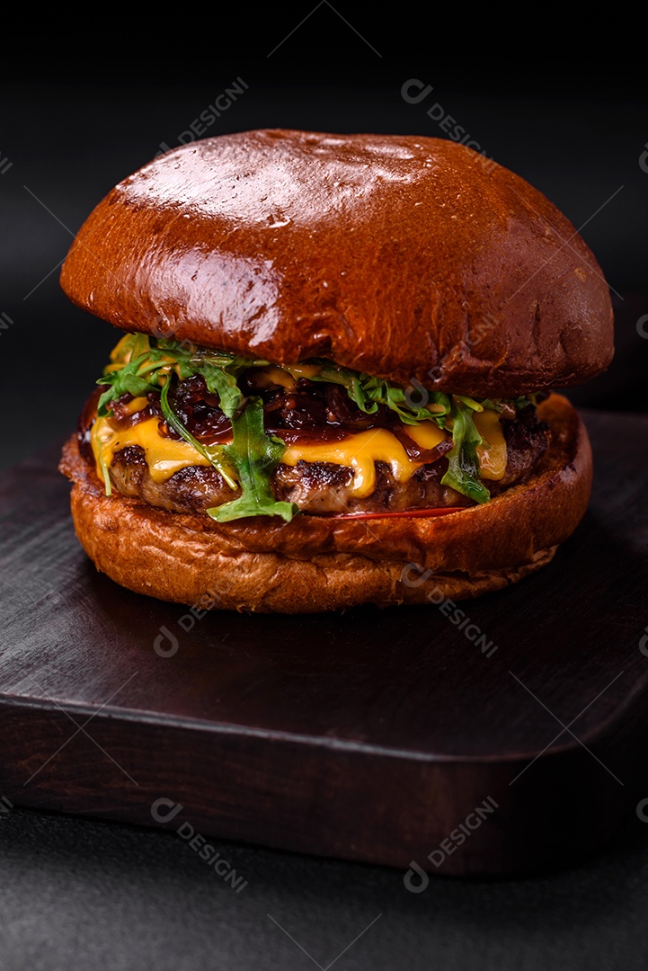 Hambúrguer com suculenta costeleta de carne, queijo, tomate, sal, especiarias e ervas sobre um fundo escuro de concreto