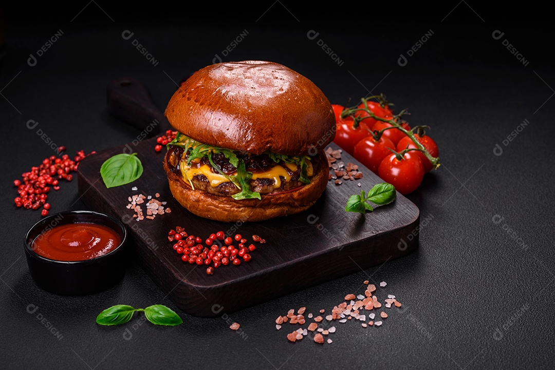 Hambúrguer com suculenta costeleta de carne, queijo, tomate, sal, especiarias e ervas sobre um fundo escuro de concreto