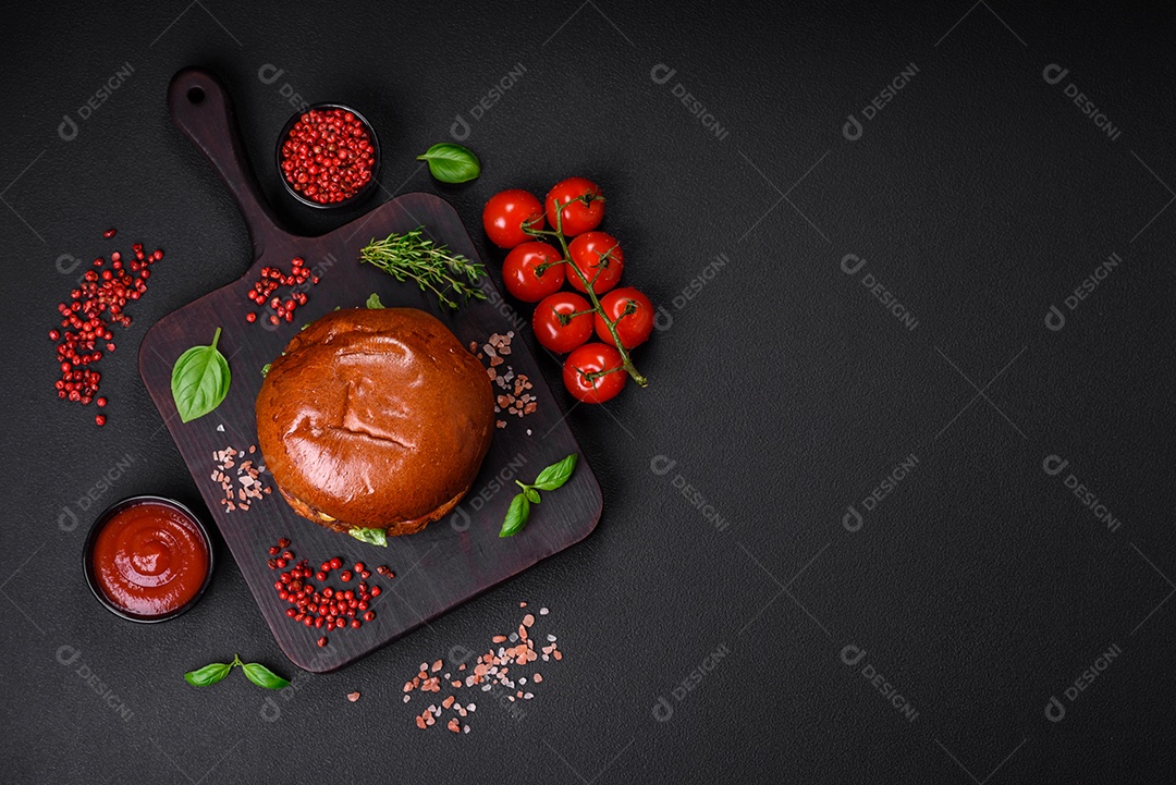 Hambúrguer com suculenta costeleta de carne, queijo, tomate, sal, especiarias e ervas sobre um fundo escuro de concreto