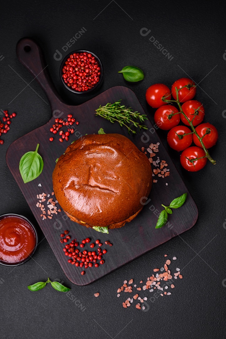 Hambúrguer com suculenta costeleta de carne, queijo, tomate, sal, especiarias e ervas sobre um fundo escuro de concreto