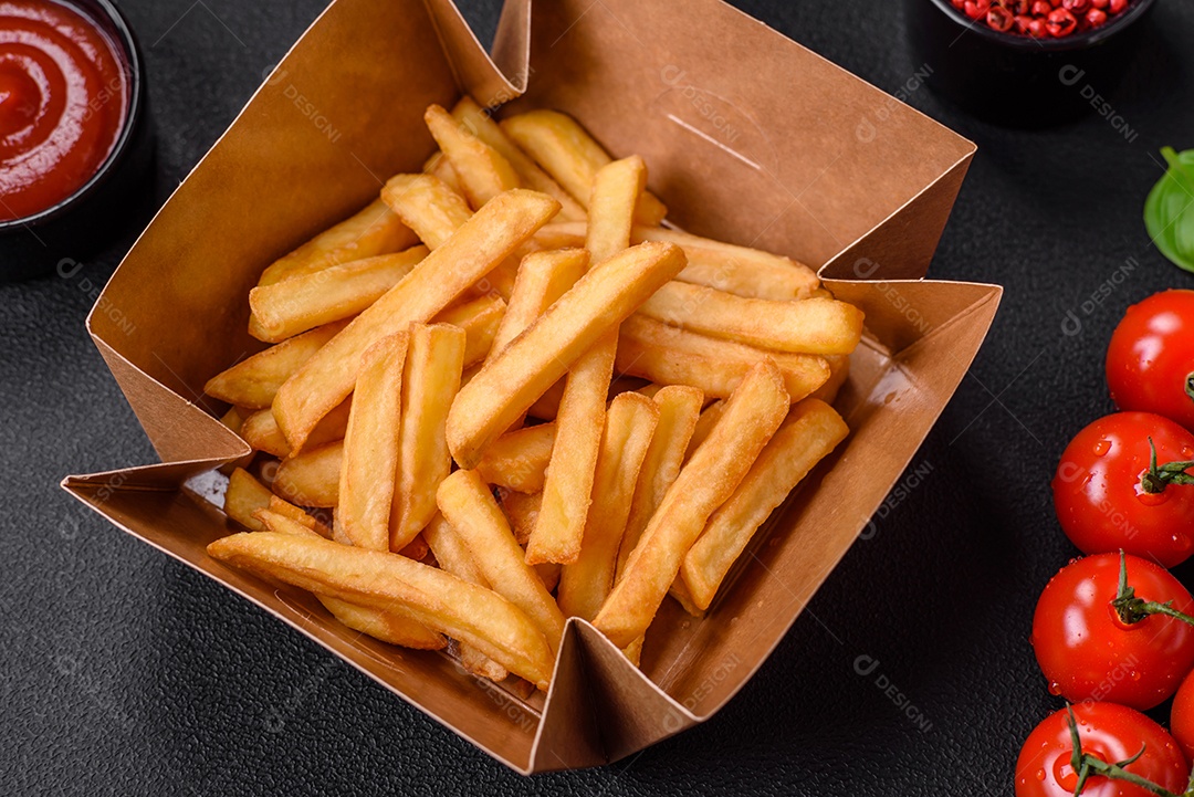 Deliciosas batatas fritas crocantes com sal e especiarias em uma caixa de papelão sobre um fundo escuro de concreto