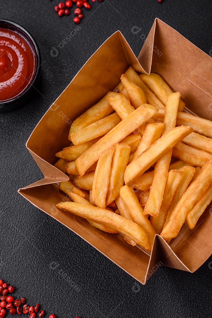 Deliciosas batatas fritas crocantes com sal e especiarias em uma caixa de papelão sobre um fundo escuro de concreto