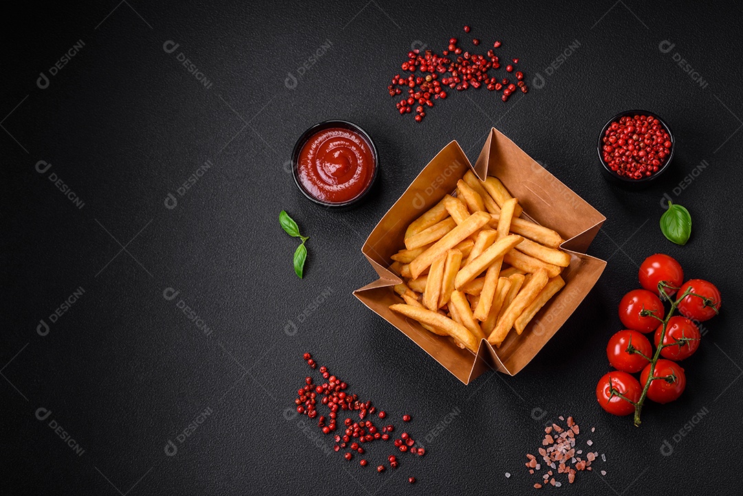 Deliciosas batatas fritas crocantes com sal e especiarias em uma caixa de papelão sobre um fundo escuro de concreto