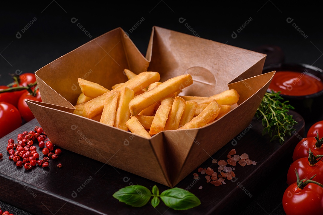 Deliciosas batatas fritas crocantes com sal e especiarias em uma caixa de papelão sobre um fundo escuro de concreto