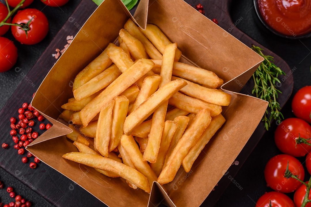 Deliciosas batatas fritas crocantes com sal e especiarias em uma caixa de papelão sobre um fundo escuro de concreto