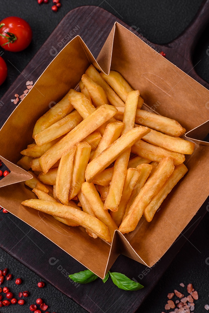 Deliciosas batatas fritas crocantes com sal e especiarias em uma caixa de papelão sobre um fundo escuro de concreto