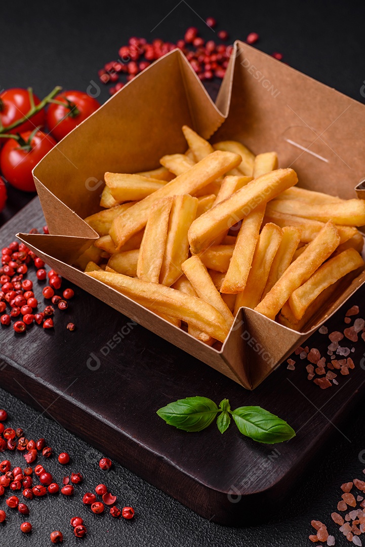 Deliciosas batatas fritas crocantes com sal e especiarias em uma caixa de papelão sobre um fundo escuro de concreto