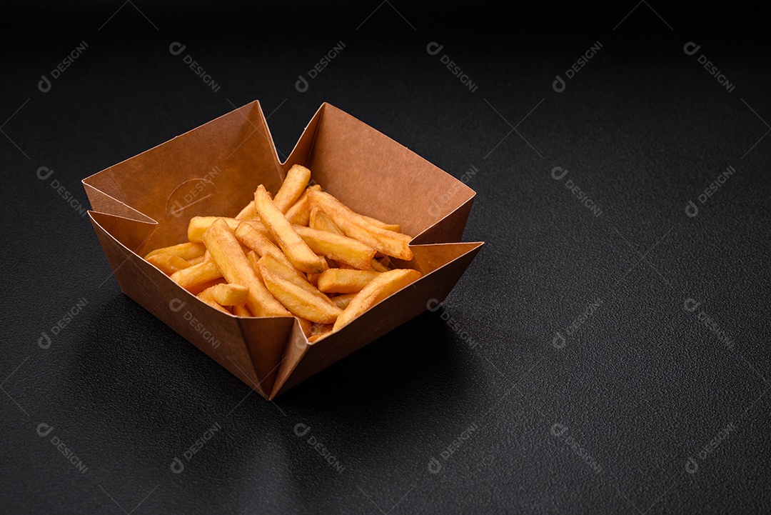 Deliciosas batatas fritas crocantes com sal e especiarias em uma caixa de papelão sobre um fundo escuro de concreto