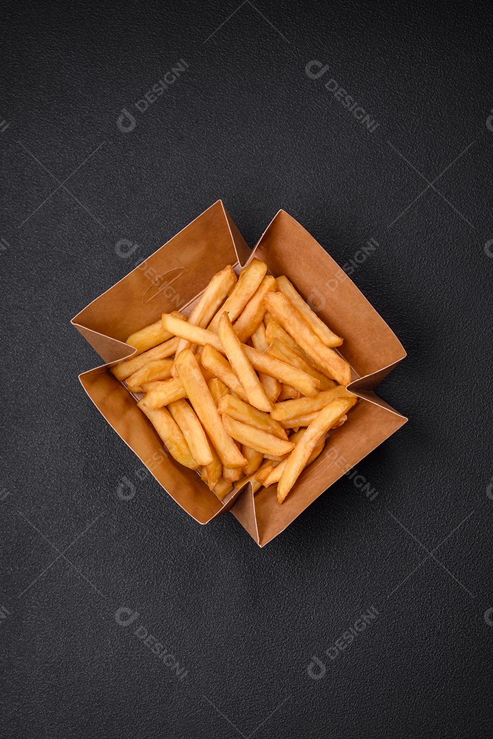 Deliciosas batatas fritas crocantes com sal e especiarias em uma caixa de papelão sobre um fundo escuro de concreto