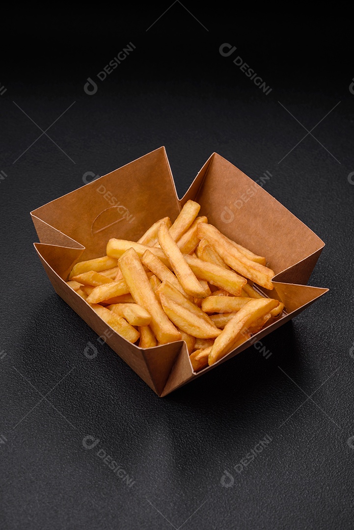 Deliciosas batatas fritas crocantes com sal e especiarias em uma caixa de papelão sobre um fundo escuro de concreto