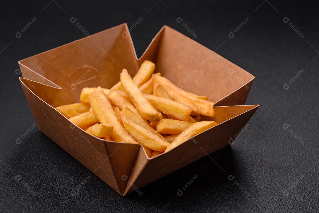 Deliciosas batatas fritas crocantes com sal e especiarias em uma caixa de papelão sobre um fundo escuro de concreto