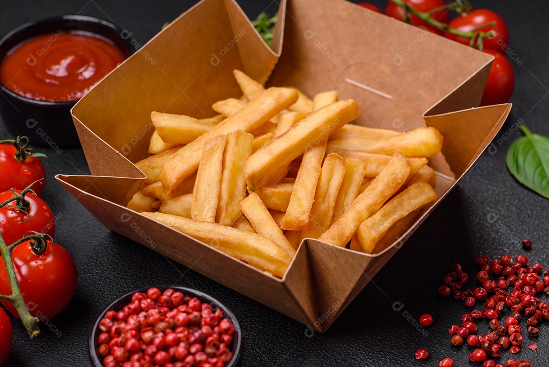 Deliciosas batatas fritas crocantes com sal e especiarias em uma caixa de papelão sobre um fundo escuro de concreto