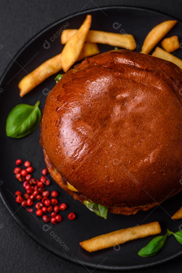 Hambúrguer com suculenta costeleta de carne, queijo, tomate, sal, especiarias e ervas sobre um fundo escuro de concreto