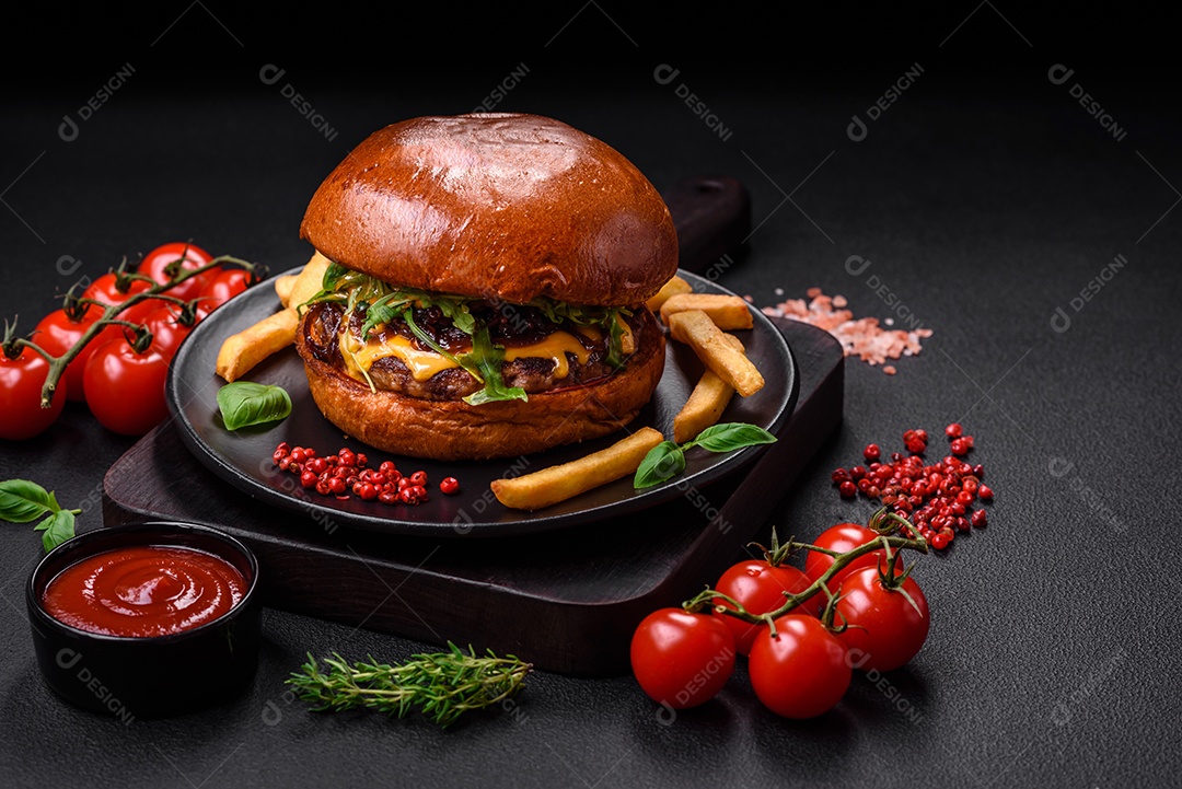 Hambúrguer com suculenta costeleta de carne, queijo, tomate, sal, especiarias e ervas sobre um fundo escuro de concreto