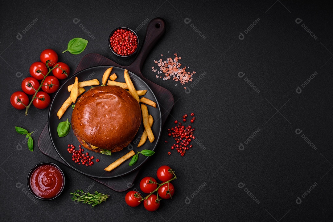 Hambúrguer com suculenta costeleta de carne, queijo, tomate, sal, especiarias e ervas sobre um fundo escuro de concreto