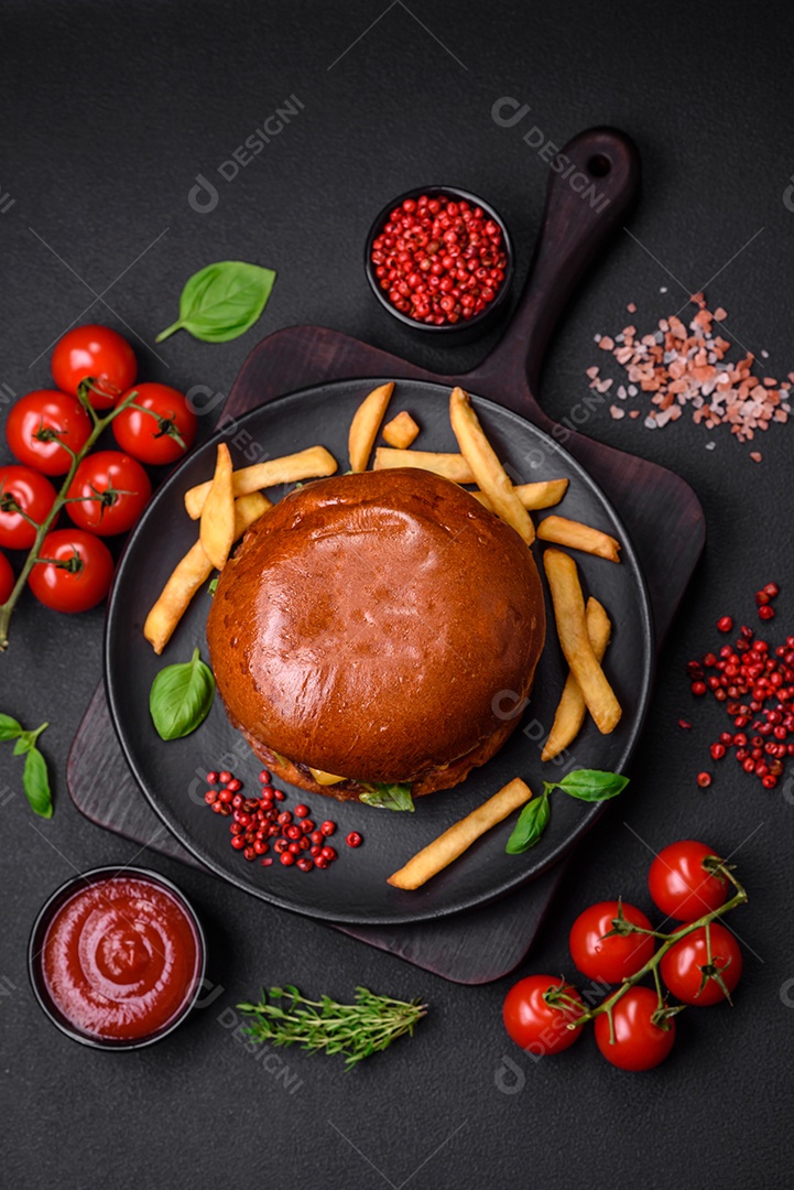 Hambúrguer com suculenta costeleta de carne, queijo, tomate, sal, especiarias e ervas sobre um fundo escuro de concreto