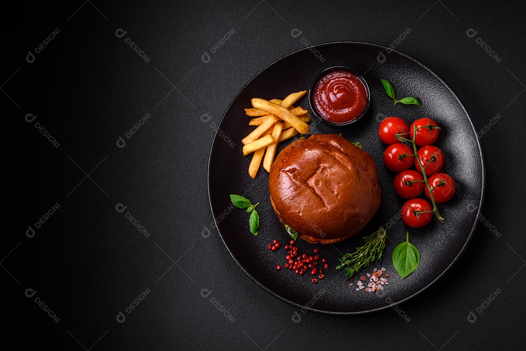 Hambúrguer com suculenta costeleta de carne, queijo, tomate, sal, especiarias e ervas sobre um fundo escuro de concreto