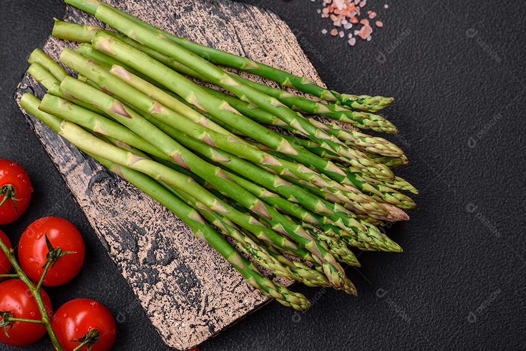 Deliciosos raminhos frescos de aspargos em um fundo escuro texturizado. Ingredientes para uma refeição vegetariana saudável