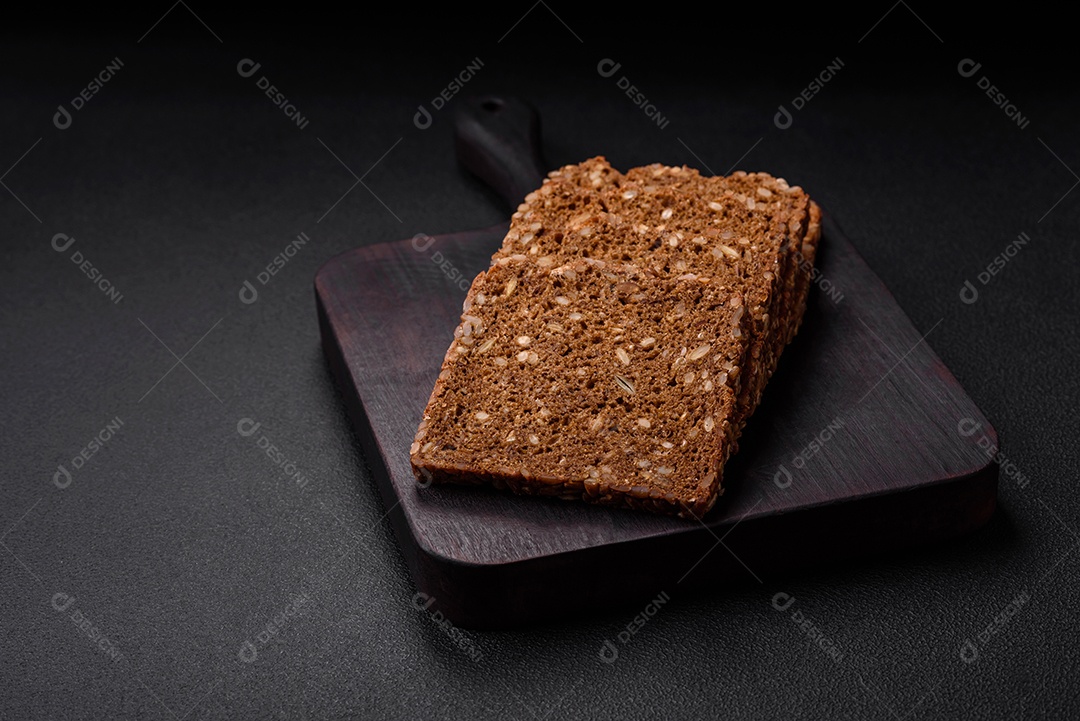 Delicioso pão integral fresco e crocante com sementes e grãos cortados em fatias sobre um fundo escuro de concreto