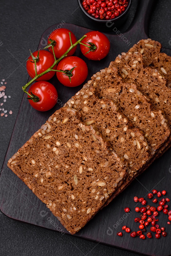 Delicioso pão integral fresco e crocante com sementes e grãos cortados em fatias sobre um fundo escuro de concreto