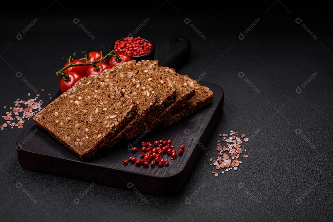 Delicioso pão integral fresco e crocante com sementes e grãos cortados em fatias sobre um fundo escuro de concreto