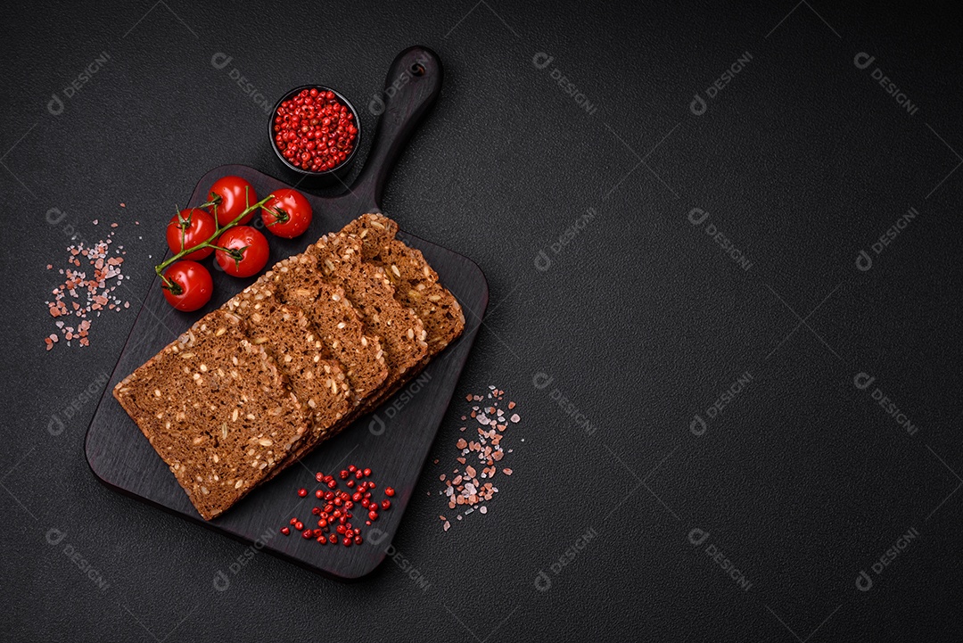 Delicioso pão integral fresco e crocante com sementes e grãos cortados em fatias sobre um fundo escuro de concreto
