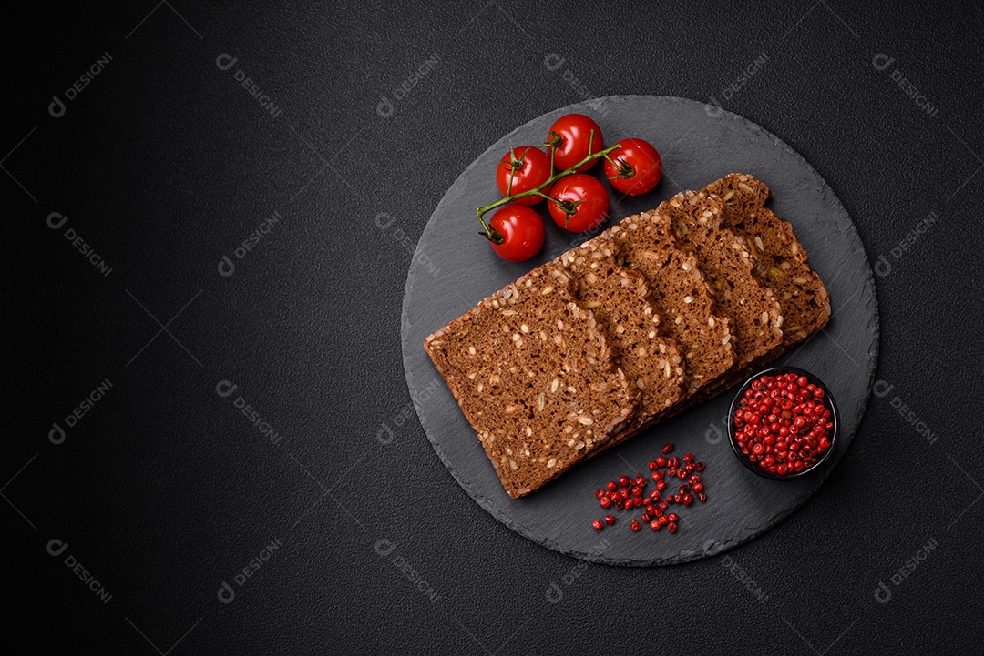 Delicioso pão integral fresco e crocante com sementes e grãos cortados em fatias sobre um fundo escuro de concreto