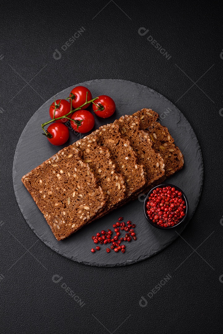 Delicioso pão integral fresco e crocante com sementes e grãos cortados em fatias sobre um fundo escuro de concreto